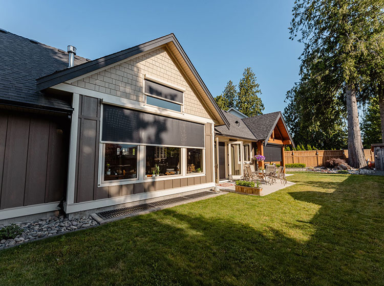 Modern craftsman exterior with dark solar shades on windows, featuring landscaped yard and outdoor seating area