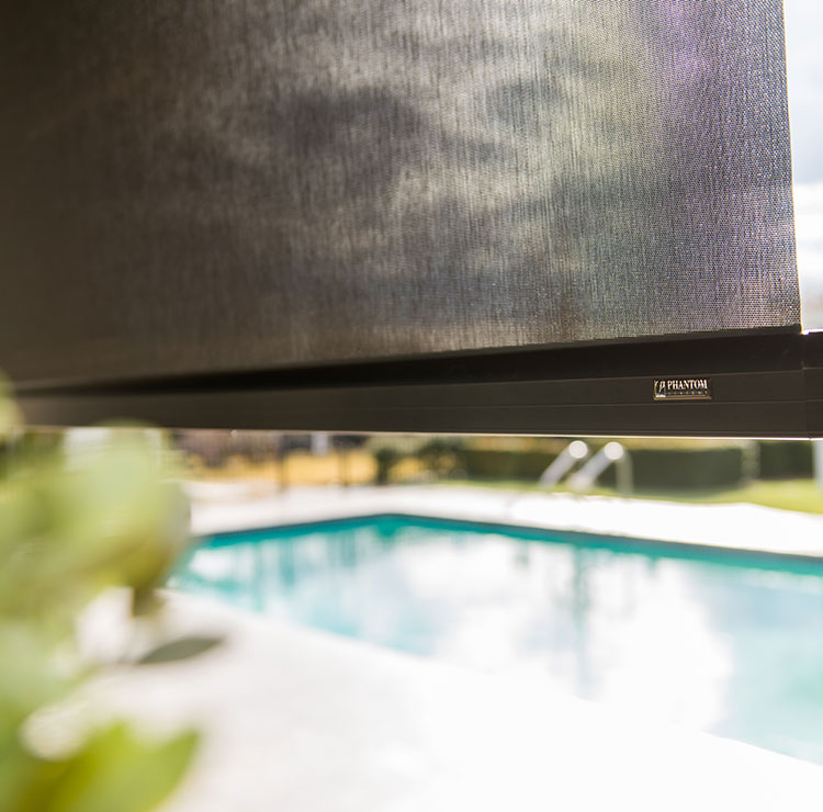 Partially lowered exterior solar shade with visible cable guide system, overlooking backyard pool and patio furniture
