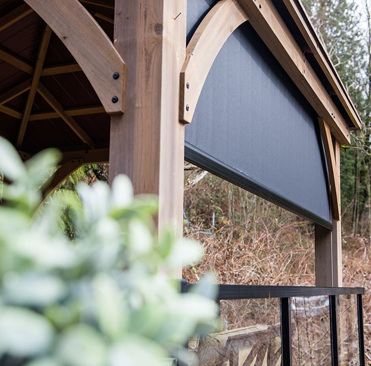 Wooden pergola with dark cable-guided screen system, mounted without corner posts against natural backdrop